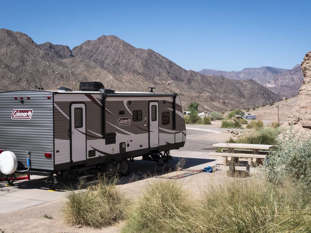An RV parked at a desert lakeside campground with mountains behind it